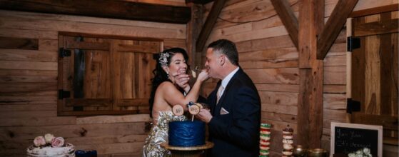 Hollow Hill Event Center Wedding and Event Venue, Weatherford, Texas. Bride and groom feeding each other cake in dark wood room with string lights on ceiling