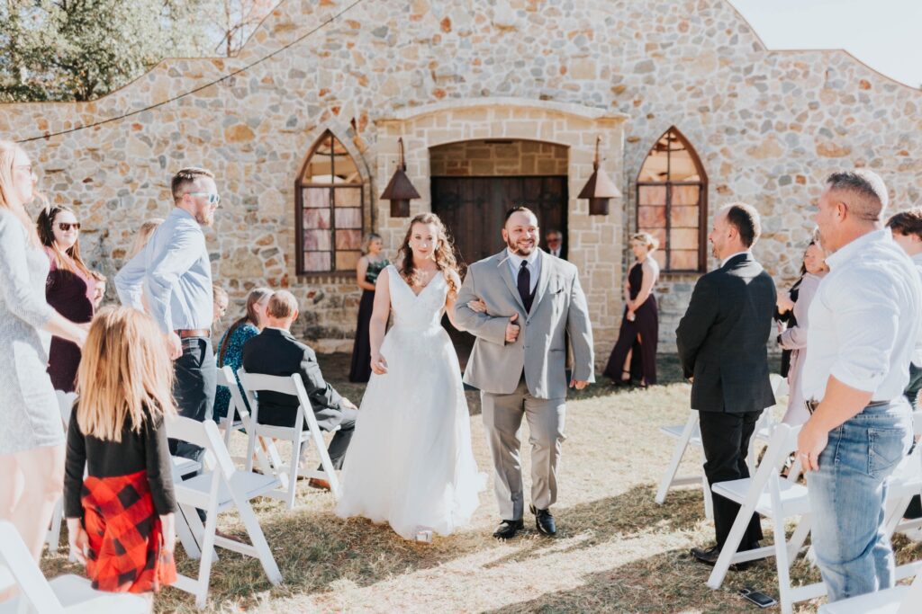 Hollow Hill Event Center Wedding and Event Venue, Weatherford, Texas. Bride and groom exiting ceremony in front of stone alamo style building