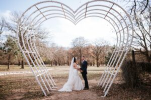 Hollow Hill Event Center Wedding and Event Venue, Weatherford, Texas. Bride and groom in clearing standing under heart shaped arch.