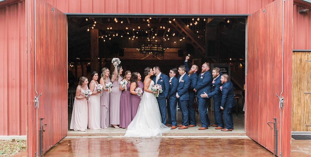 Hollow Hill Event Center Wedding and Event Venue, Weatherford, Texas. Bride and groom with wedding party in doorway of red barn.