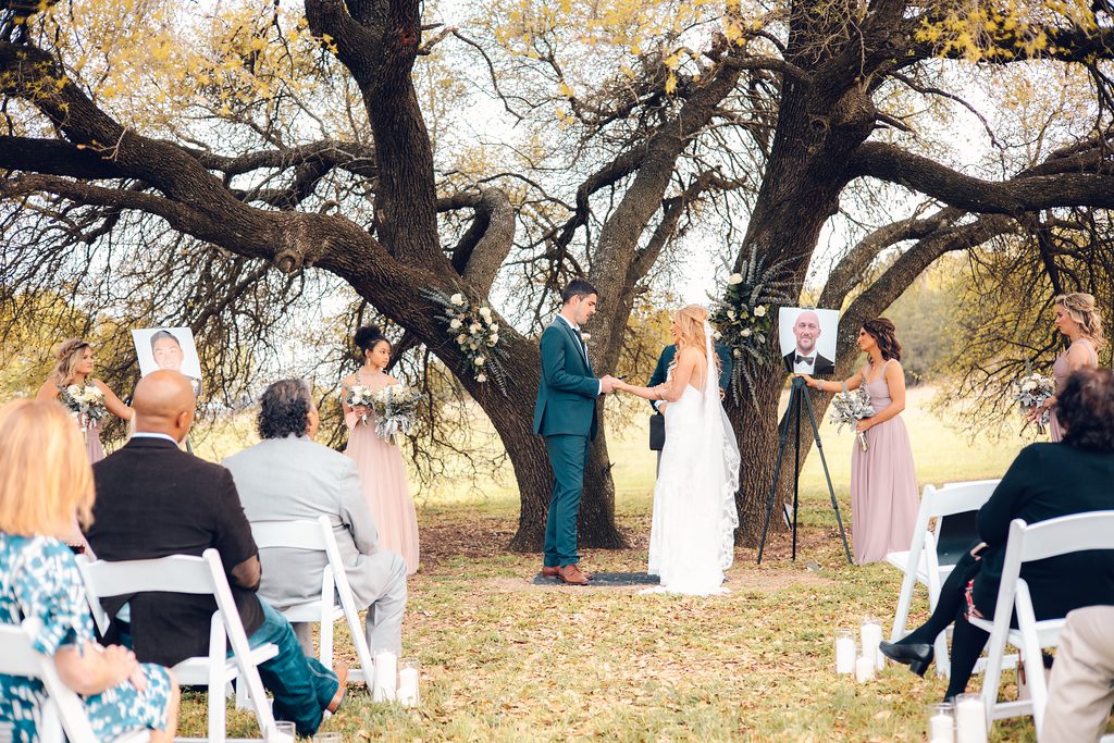 Hollow Hill Event Center Wedding and Event Venue, Weatherford, Texas. Bride and groom exchanging vows under a huge tree with guest and bridal party looking on