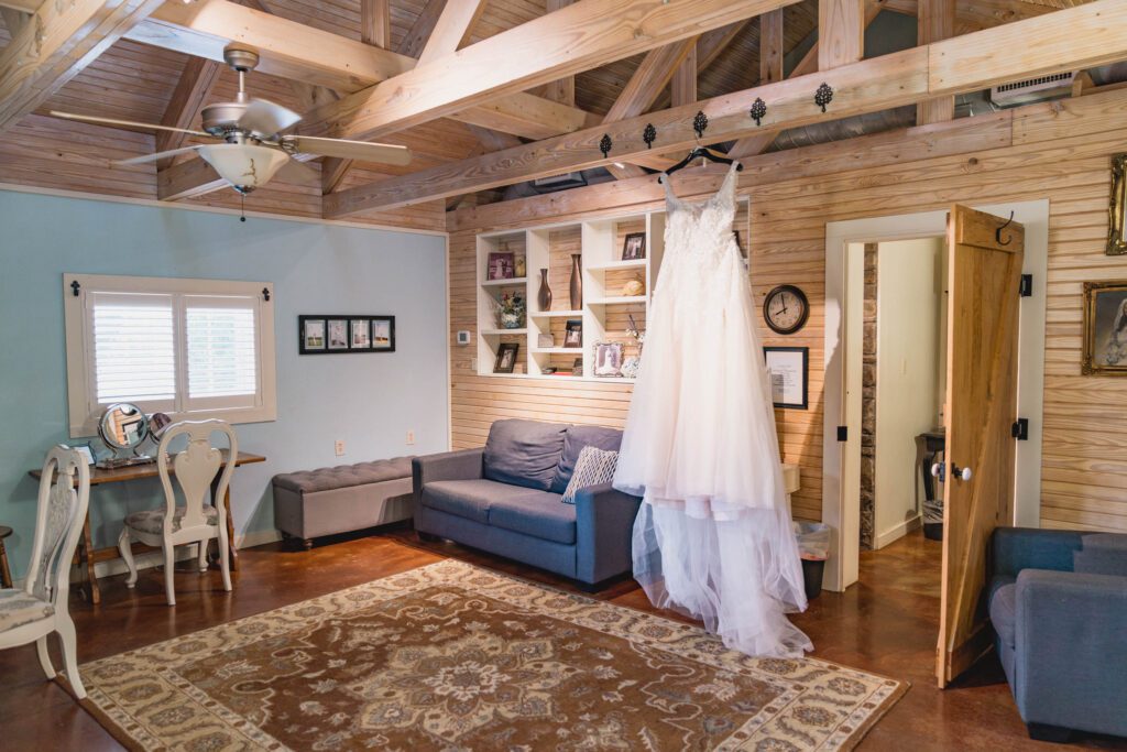 Brides Room at Hollow Hill Event Center Wedding and Event Venue, Weatherford, Texas. Room with pine walls and ceiling, sofa, chair, and vanity table. Wedding dress handing from rafter.