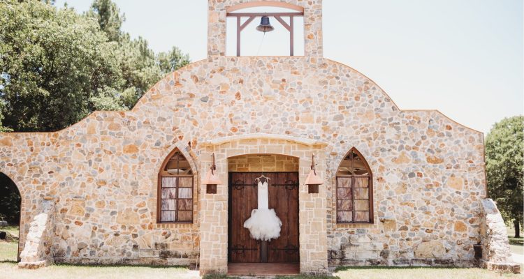 Hollow Hill Event Center Wedding and Event Venue, Weatherford, Texas. Stone alamo style building with bell tower. Wedding dress handing on front door.