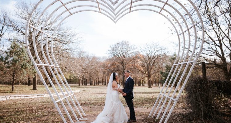 Hollow Hill Event Center Wedding and Event Venue, Weatherford, Texas. Bride and groom in clearing standing under heart shaped arch.